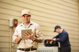 ac-technician-in-foreground-on-tablet-and-technician-in-background-looking-in-tool-bag-on-top-of-ac-unit