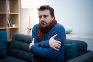 man-shivering-in-home-with-sweater-and-scarf-on