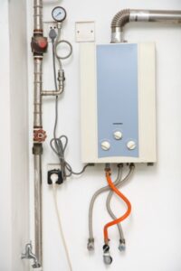 Tankless water heater installation with connected pipes and electrical wiring on a white wall.
