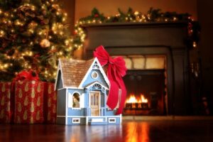 mini-house-with-red-bow-under-christmas-tree-fireplace-in-background