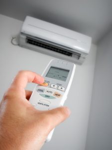 Person using remote to operate a ductless heat pump mounted on a wall.