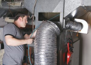 Technician performing HVAC duct cleaning with flexible hose and vacuum equipment.